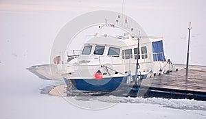 Tourist boat tied to the wooden dock on frozen river during cold