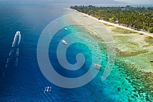 Tourist boats moored on the edge of a fringing coral reef off the coast of a tropical island at low tide