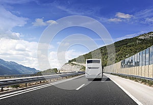 Tourist bus rushes along the country high-speed highway against the background of a mountain landscape.