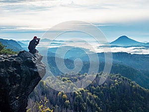 Tourist with camera in hands sit on peak of sandstone rock and watching into colorful mist