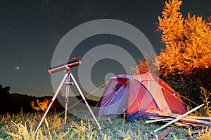 Tourist camping tent and reflector telescope on a tripod at night under starry sky