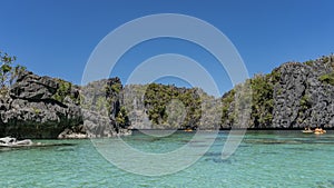 Tourist canoes sail through an amazing turquoise lagoon surrounded by picturesque karst rocks.