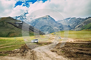 Tourist Cars SUV Go On Off Road With Views Of Mount Kazbek Near Village Of Gergeti In Georgia