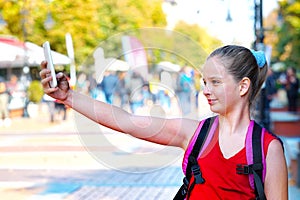 Tourist child girl with backpack taking selfies on smartphone