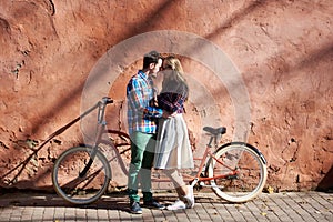 Tourist couple, bearded man and blond woman on tandem bicycle on background of red crackled wall.