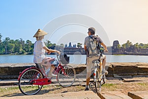 Tourist couple cycling in Angkor temple, Cambodia. Angkor Wat main facade reflected on water pond. Eco friendly tourism traveling