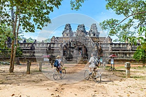 Tourist couple cycling around Angkor temple, Cambodia. Ta Keo building ruins in the jungle. Eco friendly tourism traveling