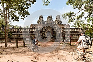 Tourist couple cycling around Angkor temple, Cambodia. Ta Keo building ruins in the jungle. Eco friendly tourism traveling, toned