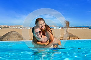 Tourist couple piggyback in infinity pool