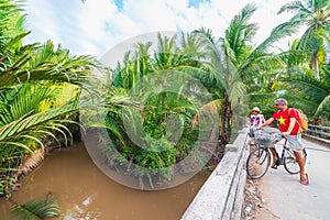 Tourist couple riding bicycle in the Mekong Delta region, Ben Tre, South Vietnam. Woman and man having fun cycling on trail among