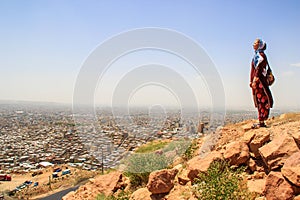 Tourist with a covered head and in a long tunic stands against the backdrop of a view of the city of Tabriz, Iran