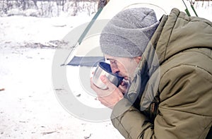 The tourist drinks hot tea in the winter forest