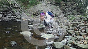 Tourist drinks from river. Close-up of girl traveler drinking water from mountain river. Stones, forest view, small pond.