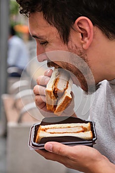 Tourist eating katsu sando at street.