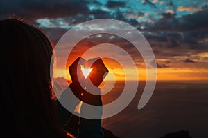 Tourist enjoy sunset at sea, making heart with hands