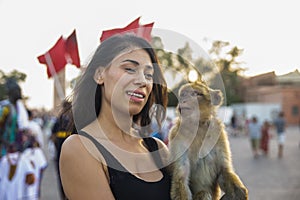 Tourist enjoying a monkey in the Jemaa el Fna square in Marrakech next to the Moroccan flag