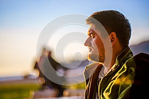 A tourist enjoys a bright sunset on the coast of the winter sea. Handsome young man in profile close-up
