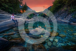 Tourist enjoys sunset at a river near stone bridge in Lavertezzo, Switzerland