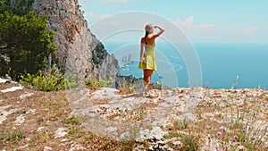 Tourist exploring the rugged terrain above Capri Island. Hiker overlooks the tranquil bay with Faraglioni rocks. Summer