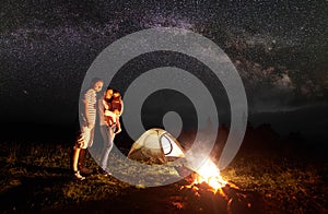 Tourist family with daughter having a rest in mountains at night under starry sky with Milky way