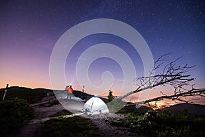 Tourist with flashlight near his camp tent at night