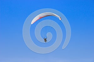 Tourist flying on a paraglider flying in the blue sky on a bight day. The sportsman paragliding