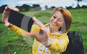 Tourist girl on background green grass taking photo selfie on mobile smart phone, person looking on camera gadget technology, blog