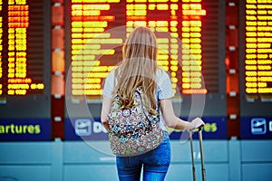 Tourist girl with backpack and carry on luggage in international airport, near flight information board