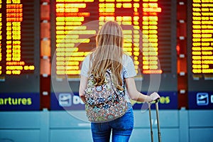 Tourist girl with backpack and carry on luggage in international airport, near flight information board photo