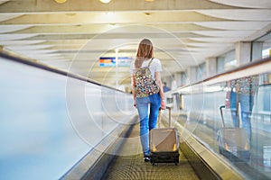 Tourist girl with backpack and carry on luggage in international airport, on travelator