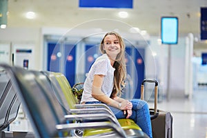 Tourist girl with backpack and carry on luggage in international airport, waiting for flight