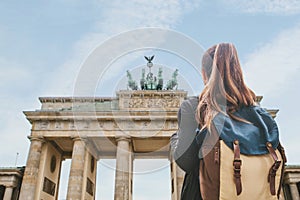 A tourist girl with a backpack looking at the Brandenburg Gate in Berlin