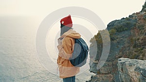 Tourist girl with a backpack standing on the edge of a cliff and enjoys a beautiful view