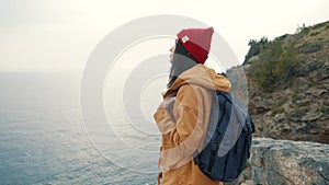 Tourist girl with a backpack standing on the edge of a cliff and enjoys a beautiful view