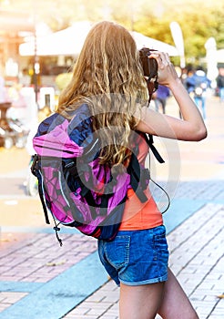 Tourist girl with backpack taking pictures on digital camera
