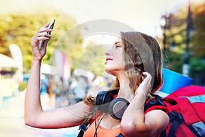 Tourist girl with backpack taking selfies on smartphone