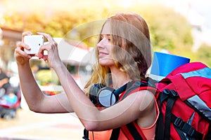 Tourist girl with backpack taking selfies on smartphone