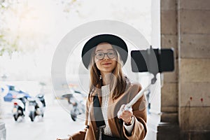 Tourist girl blogger taking photo selfie on smartphone mobile. Girl hipster travels in Barcelona. Holiday street. Traveler