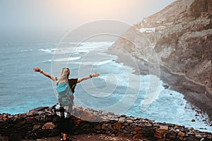 Tourist girl is happy to be on the end of long trekking route leading along cliff coastline with ocean waves from