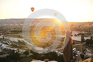 A tourist girl in a hat admires hot air balloons flying in the sky over Cappadocia in Turkey. Impressive sight.