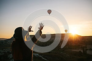 A tourist girl in a hat admires hot air balloons flying in the sky over Cappadocia in Turkey. Impressive sight.