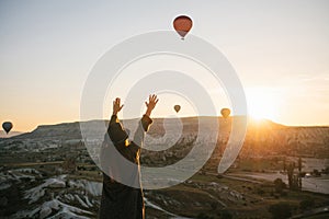 A tourist girl in a hat admires hot air balloons flying in the sky over Cappadocia in Turkey. Impressive sight.