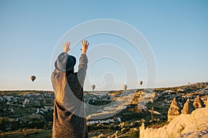 A tourist girl in a hat admires hot air balloons flying in the sky over Cappadocia in Turkey. Impressive sight.