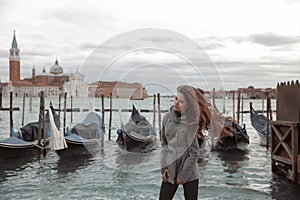 Tourist girl with long blowing hair on the pier, near the gondola spending holidays in Venice, Italy. Beautiful brunette with we