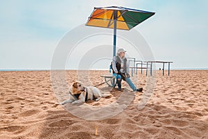tourist girl is resting with a dog under a chaise longue on an empty lonely beach