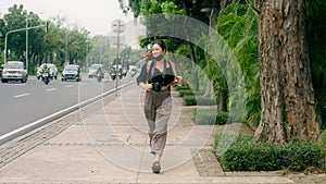 A tourist girl running with a rucksack and a camera on her chest, smiling happily with long pony tail hair winding as