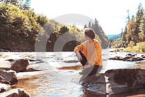 tourist girl sitting on the bank of mountain river
