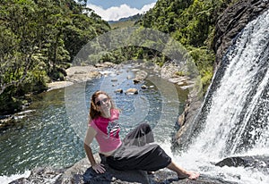 Tourist girl sitting on the rock at the edge of waterfall at the national park