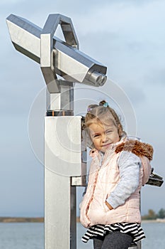 A tourist girl stands near the binoscope on the observation deck against the sky. Concept: viewing stationary binoculars for touri