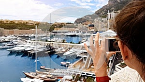 Tourist girl taking photo of yachts in Mediterranean sea port, using smartphone